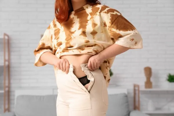 Image of woman trying to do her trousers up after pregnancy weight gain Cheshire