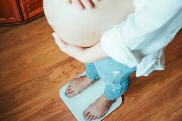 Image of woman weighing herself and experiencing weight gain through pregnancy Cheshire